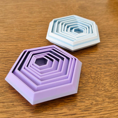 Two hexagonal fidgets in purple and blue shades, featuring layered designs, resting on a wooden surface.