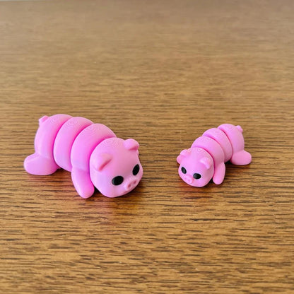 Two cute pink pigs, one larger and articulated, with black eyes, resting on a wooden surface. Perfect for sensory play.