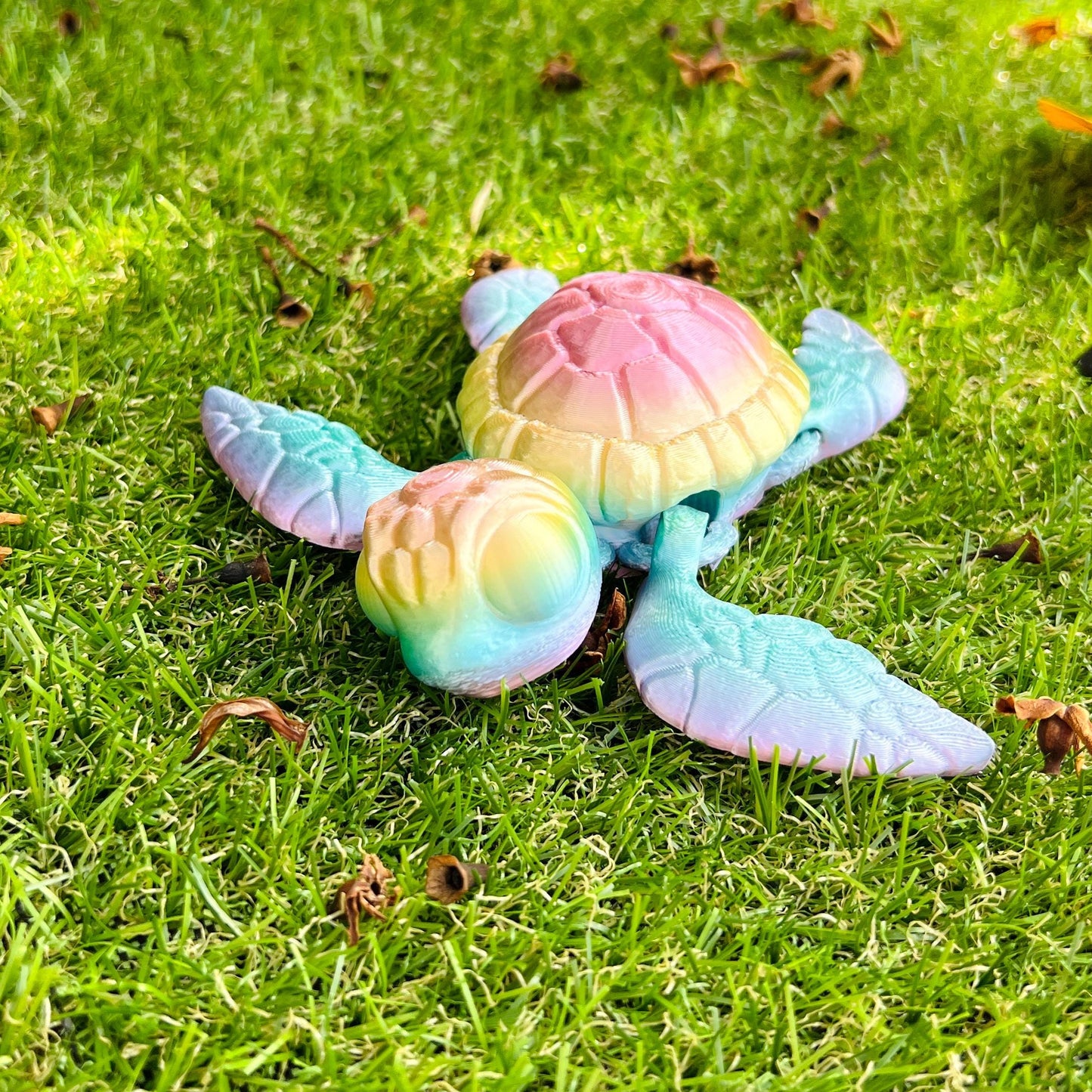 A colorful 3D-printed sea turtle figurine rests on green grass, showcasing intricate details and vibrant pastel hues.
