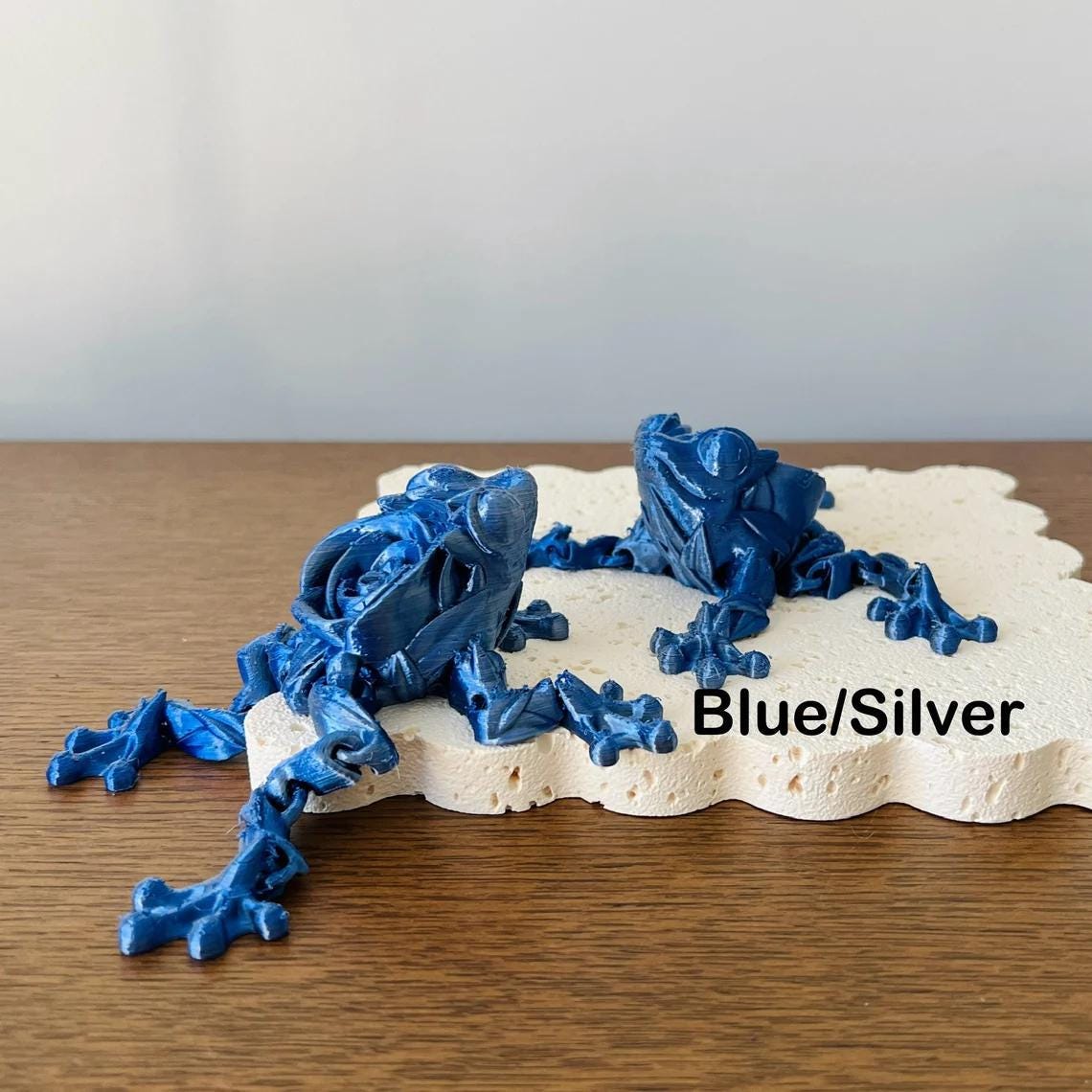 Articulated blue and silver Rose Frog figurine resting on a textured surface, showcasing intricate details and vibrant colors