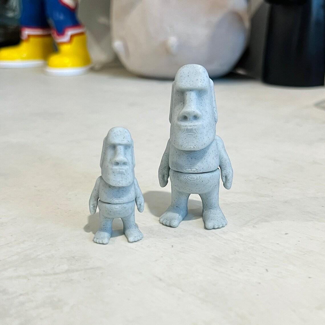 Two blue, articulated Moai figures, one smaller than the other, set against a light-colored surface.