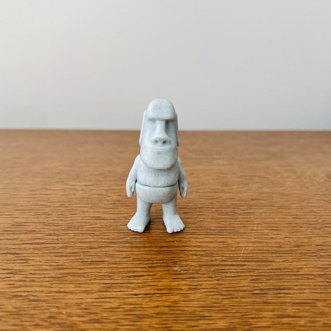 Articulated Moai figure in soft gray, standing on a wooden surface with a minimalist background for a serene aesthetic.