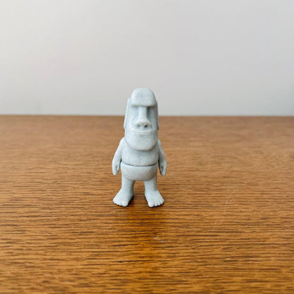 Articulated Moai figure in soft gray, standing on a wooden surface with a minimalist background for a serene aesthetic.