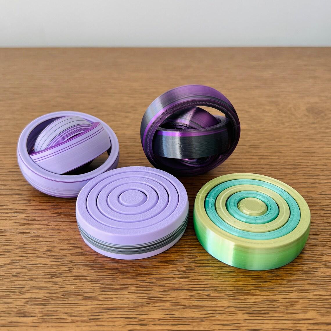 Four colorful circular fidgets in purple, green, and multicolored blends, resting on a wooden surface.