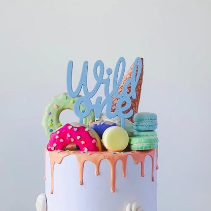 Colorful cake topper reading "Wild one" above vibrant sweets and dripping icing, perfect for a playful celebration.