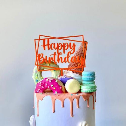 Large orange "Happy Birthday" topper with colorful sweets on a white frosted cake, enhancing the festive atmosphere.