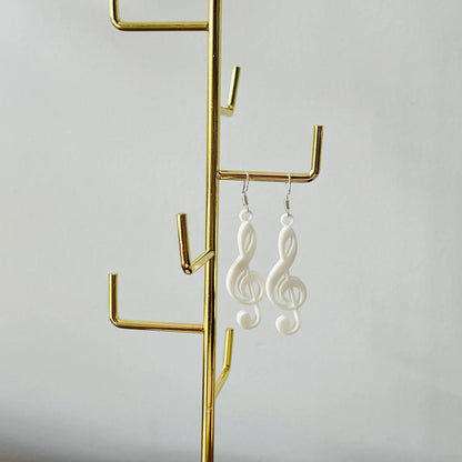 Elegant white treble clef dangle earrings hanging on a gold display stand against a light backdrop.