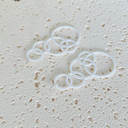 White bubble dangle earrings with multiple circular layers, hanging from sterling silver hooks, on a textured surface.