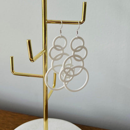 White bubble dangle earrings hang elegantly on a gold display stand, showcasing their playful, modern design.