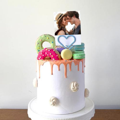 Colorful cake adorned with donuts and macarons, featuring a photo holder in the shape of a heart for special memories.