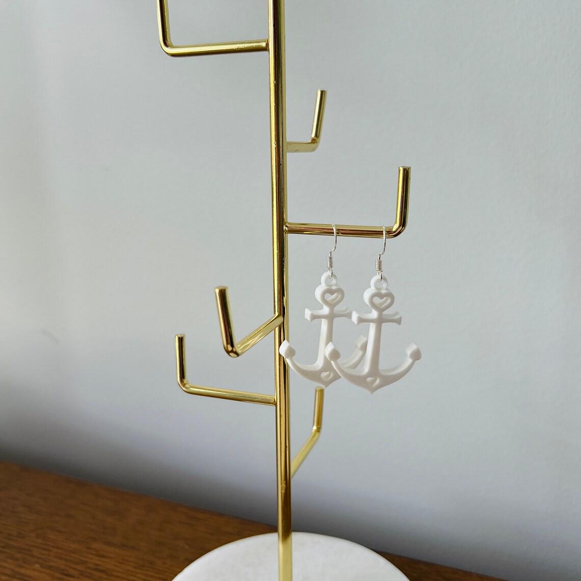 Elegant white anchor dangle earrings hanging from a gold display stand, showcasing their lightweight and stylish design.