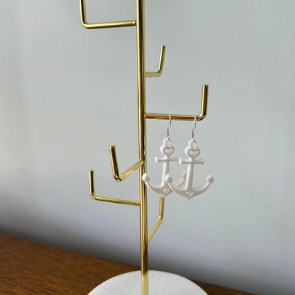 Elegant white anchor dangle earrings hanging from a gold display stand, showcasing their lightweight and stylish design.