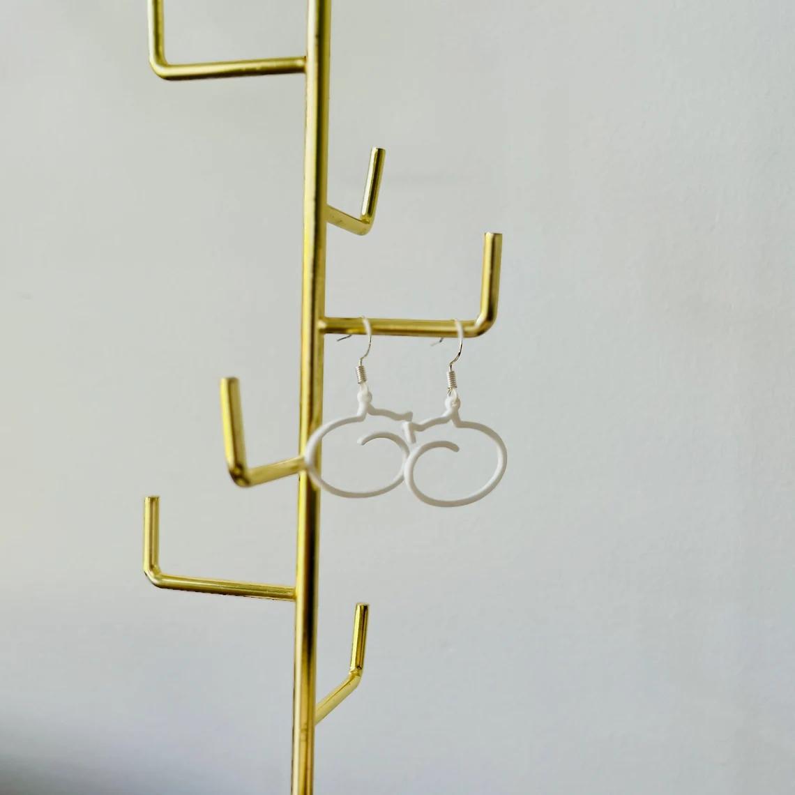 Whimsical cat dangle earrings in lightweight white plastic, hanging from a gold display, perfect for cat lovers.