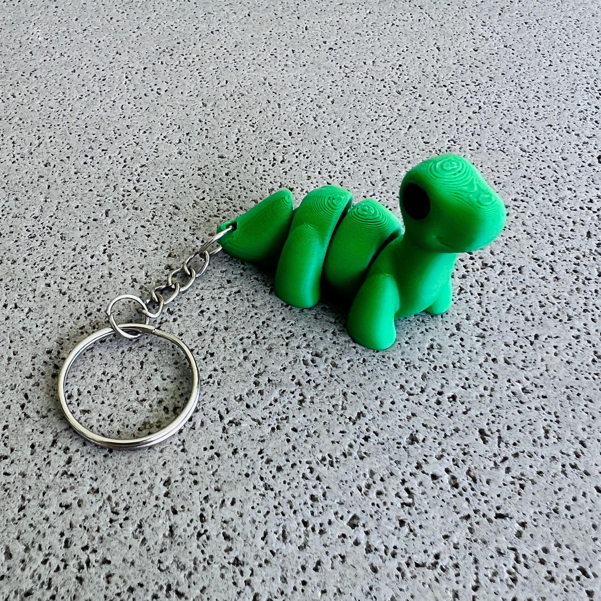 Charming green Brontosaurus keychain with a shiny keyring, perfect for adding flair to bags or keys. Ideal for dino lovers!