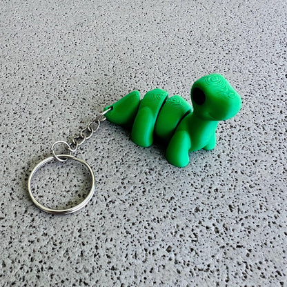 Charming green Brontosaurus keychain with a shiny keyring, perfect for adding flair to bags or keys. Ideal for dino lovers!