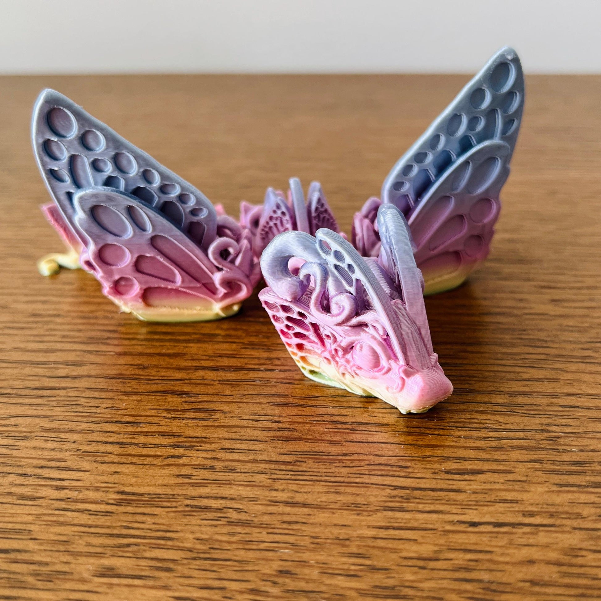 Delicate Butterfly Dragon Tadling with intricate, colorful wings resting on a wooden surface, showcasing whimsical charm.