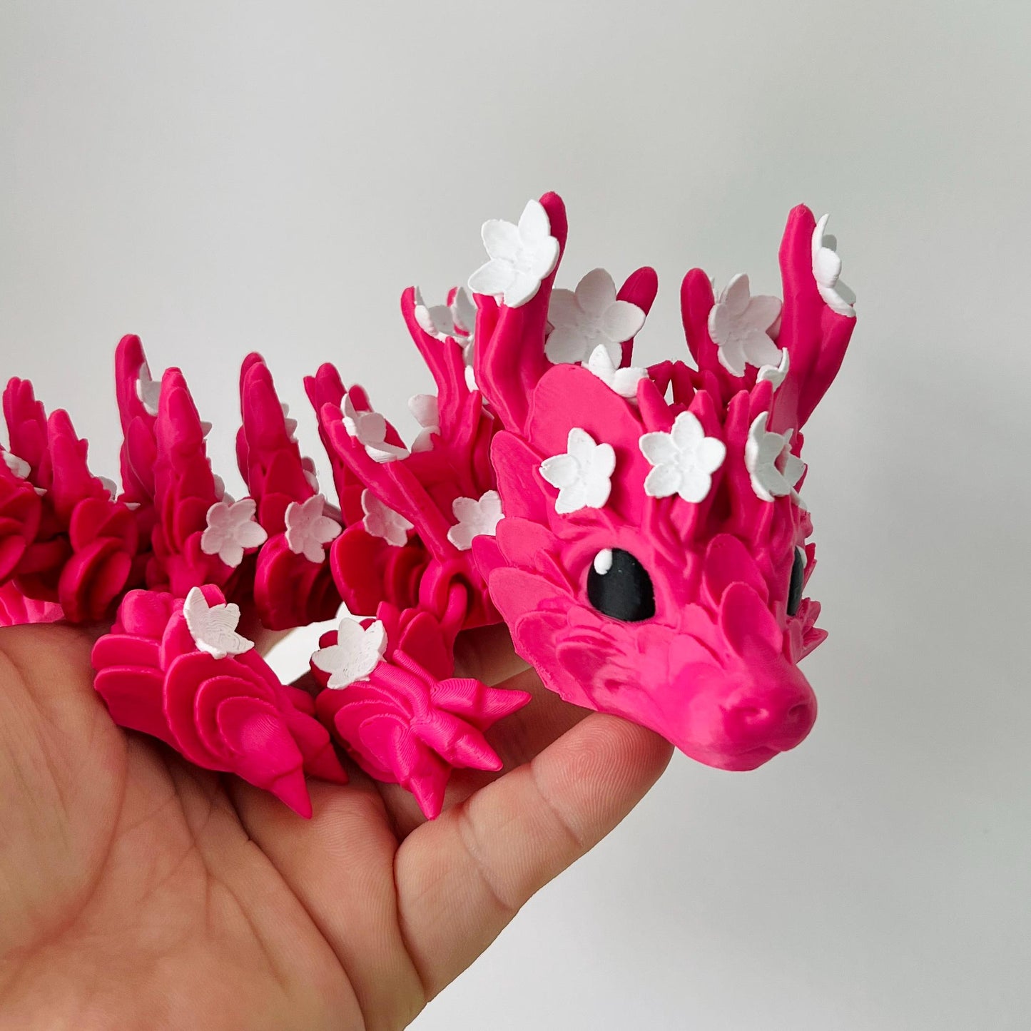 A vibrant pink dragon adorned with white cherry blossom petals, showcasing intricate details and a whimsical expression.