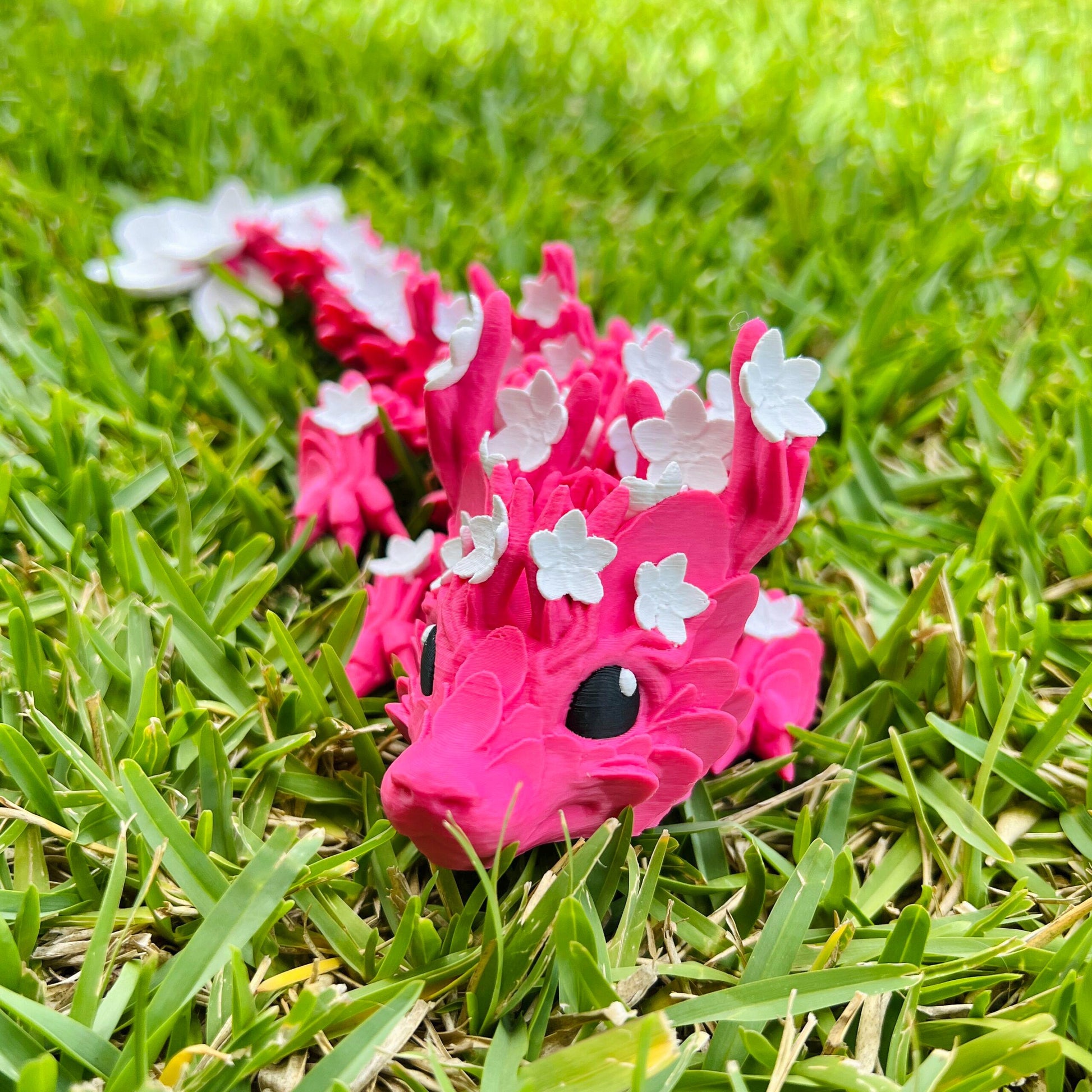 A vibrant pink dragon adorned with delicate white cherry blossoms, resting gracefully on lush green grass.