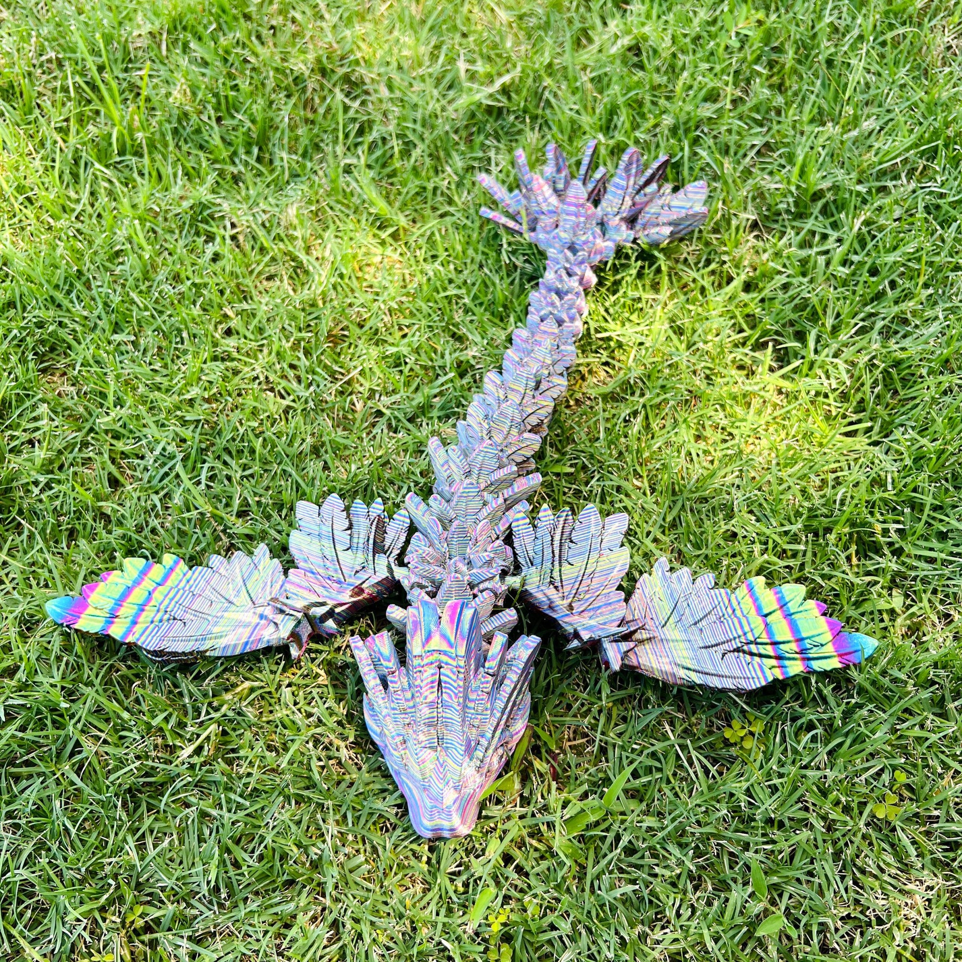 A sleek, iridescent winged dragon with intricate scales and vibrant colors, resting on lush green grass.